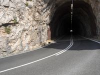 the road is curved and has two white lines going in both directions to the left of the tunnel