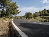 the road is made out of asphalt with trees on both sides of it and a bright blue sky above