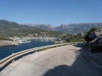 the road curves by the mountains over the ocean and mountains in the distance are filled with boats