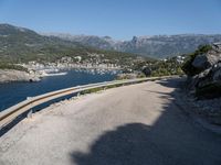 the road curves by the mountains over the ocean and mountains in the distance are filled with boats