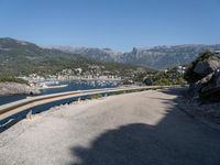 the road curves by the mountains over the ocean and mountains in the distance are filled with boats