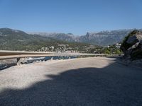 the road curves by the mountains over the ocean and mountains in the distance are filled with boats