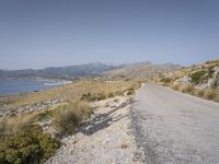 a person on their bike down the road in front of water and land with mountains in the background