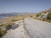 a person on their bike down the road in front of water and land with mountains in the background