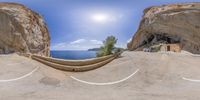 a curved stone walkway that runs past a mountain cliff next to the ocean and water