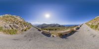 a fisheye lens of a mountain and a road with grass and bushes on it