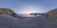 a road on a mountain side with the ocean in the background and a plane landing