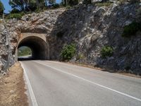 road going into the entrance of an old stone cave and a steep cliff formation overhang