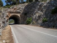 road going into the entrance of an old stone cave and a steep cliff formation overhang