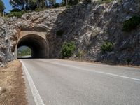 road going into the entrance of an old stone cave and a steep cliff formation overhang