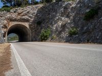 road going into the entrance of an old stone cave and a steep cliff formation overhang