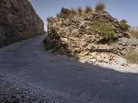 a road leading the side of a steep rock wall between two hills with tall grass growing up on the rocks