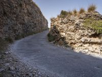 a road leading the side of a steep rock wall between two hills with tall grass growing up on the rocks