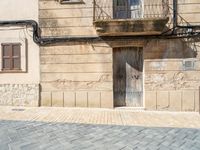 a door in an old stone building with a balcony next to it, and a street with stone brick pavers