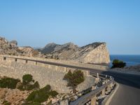 a curved road is next to a rocky cliff cliff side under a blue sky with two people on it