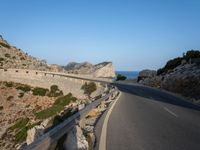 a curved road is next to a rocky cliff cliff side under a blue sky with two people on it