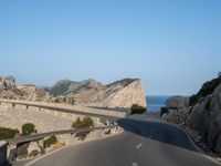 a curved road is next to a rocky cliff cliff side under a blue sky with two people on it