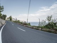 a winding road on a clear day with the ocean visible in the background, with bushes and trees around the curve,