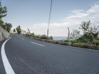 a winding road on a clear day with the ocean visible in the background, with bushes and trees around the curve,