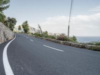 a winding road on a clear day with the ocean visible in the background, with bushes and trees around the curve,