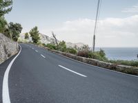 a winding road on a clear day with the ocean visible in the background, with bushes and trees around the curve,