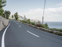 a winding road on a clear day with the ocean visible in the background, with bushes and trees around the curve,