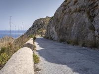 there is a rock wall at the edge of the cliff by the water on the road