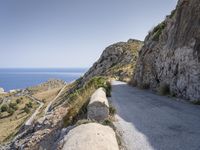 there is a rock wall at the edge of the cliff by the water on the road