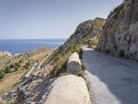 there is a rock wall at the edge of the cliff by the water on the road