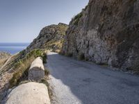 there is a rock wall at the edge of the cliff by the water on the road