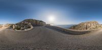 a panorama looking down at a road next to a cliff with water and a body of water in the background