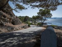 an empty country road with rocks and trees on the side of it with a sea view