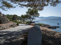 an empty country road with rocks and trees on the side of it with a sea view