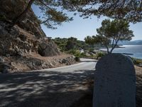 an empty country road with rocks and trees on the side of it with a sea view