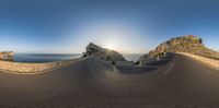 an empty road curves under the sun as it passes behind a large rock formation on a cliff