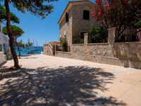 a stone building next to the water and a small tree and bushes in front of it