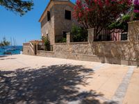 a stone building next to the water and a small tree and bushes in front of it