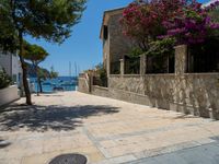 a stone building next to the water and a small tree and bushes in front of it