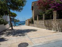 a stone building next to the water and a small tree and bushes in front of it