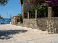 a stone building next to the water and a small tree and bushes in front of it