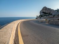 a curved road stretches to a mountain near the ocean on a sunny day with no clouds