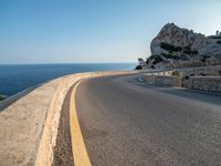 a curved road stretches to a mountain near the ocean on a sunny day with no clouds