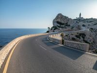 a curved road stretches to a mountain near the ocean on a sunny day with no clouds