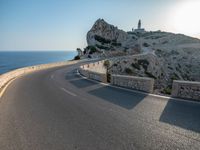 a curved road stretches to a mountain near the ocean on a sunny day with no clouds