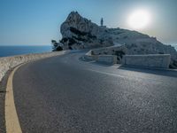 a curved road stretches to a mountain near the ocean on a sunny day with no clouds