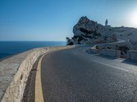 a curved road stretches to a mountain near the ocean on a sunny day with no clouds