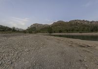 a group of rocks sits in the river bank surrounded by green trees and mountains on either side