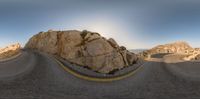 a road going around some rocks and rocks with the sun shining in the background in the middle