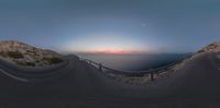 the curved road leads up to a mountain top at sunset with ocean behind it and mountains in the distance