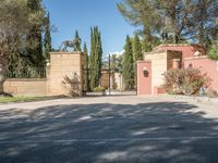 a driveway with some trees and some stone walls and a fence and gates with a statue of a horse